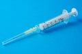 Close-up of transparent plastic syringe, with needle covered, on blue background horizontally