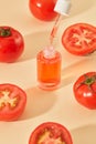 Close-up of a transparent serum bottle filled with orange liquid. Beige background with fresh tomatoes and tomato halves. Concept