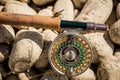 A close up of a trout fly rod, reel and line on rocks, with a cicada fly