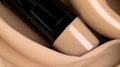 a close up of a tube of foundation cream on a cloth with a beige cloth around it and a black tube of foundation cream on the top
