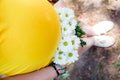 Close up on tummy of pregnant woman, wearing yellow dress, holding in hands bouquet chamomile flowers outdoors, new life concept. Royalty Free Stock Photo