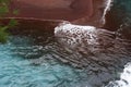Close up of the turquoise water of the Pacific Ocean rolling onto the red sand of the Red Sand Beach on Kaihalulu Bay