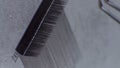 Close up of tweezers in hand of unrecognizable lashmaker running tip of tool over black false eyelashes in palette.