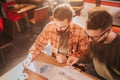 Close up of two adult and bearded guys sitting at the table and studying graphics in documents. They are preparing for