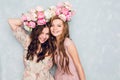 Close-up of two beautiful girls stand in a studio,who play silly with circlets of flowers on their heads. They wear