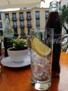 Close up of two bottles of coca cola with text in spanish on a cafe table with a glass containing ice cubes and a slice of lemon