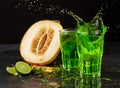 Close-up of two bright tarragon splashing cocktails on a black background. Green tarragon, cut melon, and sour lime.