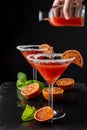 Close-up of two cocktail glasses with blood orange martini and hand with bottle and liquid, out of focus which is going to serve Royalty Free Stock Photo