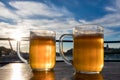 Close-up two cold beers with foam and water drops on the background blue sky and white clouds and the sun