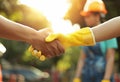 Close up of two construction workers shaking hands with other people in the background, sunny day, worker wearing a Royalty Free Stock Photo