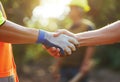 Close up of two construction workers shaking hands with other people in the background, sunny day, worker wearing a Royalty Free Stock Photo