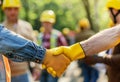 Close up of two construction workers shaking hands with other people in the background, sunny day, worker wearing a Royalty Free Stock Photo