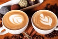 Two cappuccino cups with latte-art on a wooden table with scattered coffee beans and cakes. Joy with a Cup of coffee Royalty Free Stock Photo
