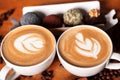 Two cappuccino cups with latte-art on a wooden table with scattered coffee beans and cakes. Joy with a Cup of coffee Royalty Free Stock Photo