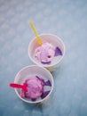 Close-up of two cups of lilac ice cream with syrup and color spoons stand on the table