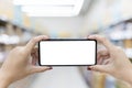 Close up of two female hands holding a mobile phone on a horizontal blank white screen. Blurred supermarket background Royalty Free Stock Photo