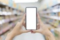 Close up of two female hands holding a mobile phone on a vertical blank white screen. Blurred supermarket background. Mockup Royalty Free Stock Photo