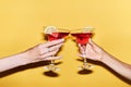 Close up of two female hands holding red cocktails against yellow background Royalty Free Stock Photo