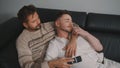 Close up. Two gay men in casual outfits sitting on sofa embracing and watching TV at home Royalty Free Stock Photo