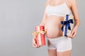 Close up of two gift boxes in pregnant woman`s hands against her belly at gray background. Is it a boy or a girl Waiting for twin Royalty Free Stock Photo