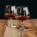 Close up of two glass goblets with alcohol resting on a wooden table against a dark background