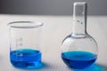 Close-up of two glass test tubes with blue liquid, on white wooden table and gray background, horizontally