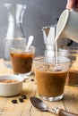 Close-up of two glasses with ice coffee, jug pouring milk, spoon, coffee beans, brown sugar with coffee pot and bottle of water, w Royalty Free Stock Photo