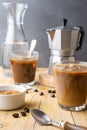 Close-up of two glasses with ice coffee, spoon, coffee beans, brown sugar with coffee pot and bottle of water, with selective focu Royalty Free Stock Photo