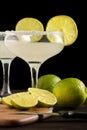 Close-up of two glasses with margarita cocktail, on dark wooden table with table, knife, limes and lemons, black background Royalty Free Stock Photo