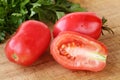Close up of two and a half fresh, organic pink plum tomatoes on a wooden cutting board, blurred parsley in the background. Royalty Free Stock Photo