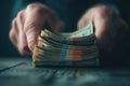 hands organizing a thick stack of banded hundred-dollar bills on a dark wooden surface in moody lighting Royalty Free Stock Photo
