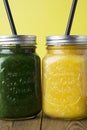 Close up two jars with green and yellow detox smoothie with straws. Spinach and pumpkin smoothie on wooden table