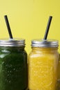 Close up two jars with green and yellow detox smoothie with straws. Spinach and pumpkin smoothie on wooden table