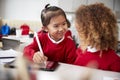 Close up of two kindergarten schoolgirls wearing school uniforms, sitting at a desk in a classroom using a tablet computer and sty Royalty Free Stock Photo