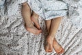 Close-up of two pairs of toddler girls feet on the bed under the blanket. Light blue and beige tones