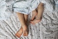 Close-up of two pairs of toddler girls feet on the bed under the blanket. Light blue and beige tones Royalty Free Stock Photo