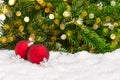 Close-up of two red Christmas balls and snowflakes on snow with fir tree branches and bokeh lights in the background Royalty Free Stock Photo