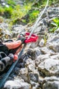 Close up of two red locking carabiners being pushed up along a steel wire by a male hand with cutout gloves, on a via ferrata