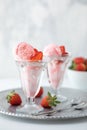 Two strawberry ice cream sundaes on a metal tray with a bowl of strawberries in behind.
