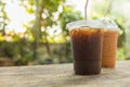 Close up of two take away plastic cup of iced black coffee Americano and iced milk tea on wooden table in garden with green leaf Royalty Free Stock Photo