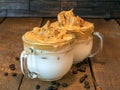 Close-up of two Dalgona Whipped coffee drinks in a Clear coffee mug with milk on a wooden background.