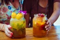 Close up of two women in colourful dresses holding glasses with refreshing strawberry apple cocktail with lime and peach Royalty Free Stock Photo