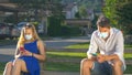 CLOSE UP: Two strangers wear facemasks while sitting on park bench and texting.