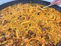 close up of a typical Valencian paella, typical food of the Spanish Levante, a hand serving a plate of paella at the edge of the