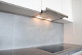 A close-up on under cabinet range hood, exhaust vent hood with lights working and modern electric stove, cooktop in gray and white Royalty Free Stock Photo