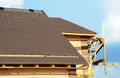 A close-up on unfinished roofing construction, covered with dimensional asphalt roof shingles, and brick walls of the house with