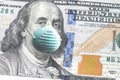 Close up of United States paper currency one hundred dollar bill with Benjamin Franklin wearing blue face mask due to COVID-19