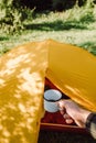 Close up of unknown young man holding hot coffee cup in summer morning, enjoying hike. Beautiful shadows of leafy tree foliage