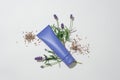 Close-up of an unlabeled purple cosmetic tube placed on a white background with fresh and dried lavender flowers. Lavender is a