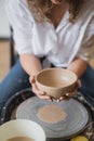 Close up of unrecognizable ceramist forming handcrafted clay vase using special tool and potter circle.